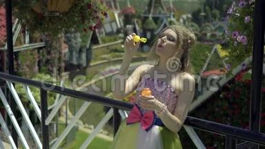年轻的金发女人在花园里吹肥皂泡。 漂亮的梦想可爱的女孩穿着滑稽的蕾丝礼服放松